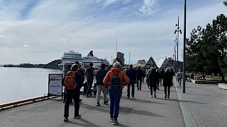 Bildet viser himmel, hav og personer på vandring bryggelangs